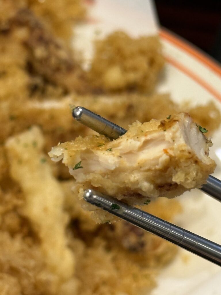Juicy fried chicken tenderloin held up with chopsticks