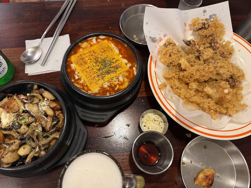 Table full of tteokbokki, fried squid and draft beer