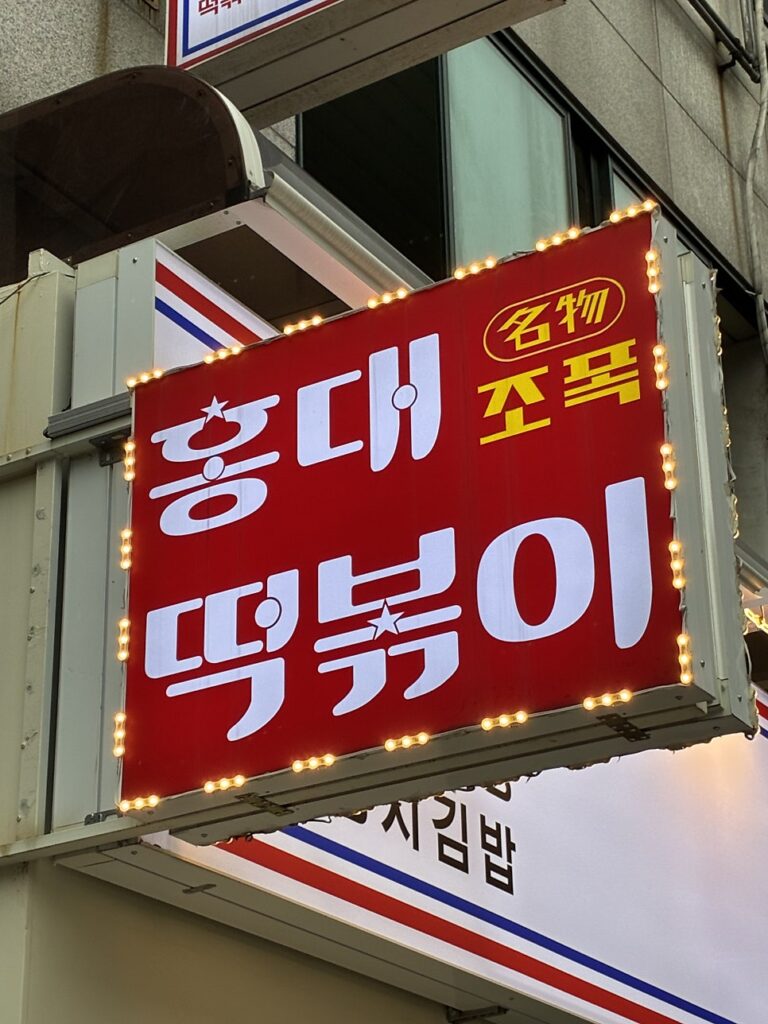 Red Hongdae Jopok Tteokbokki sign glowing outside the shop
