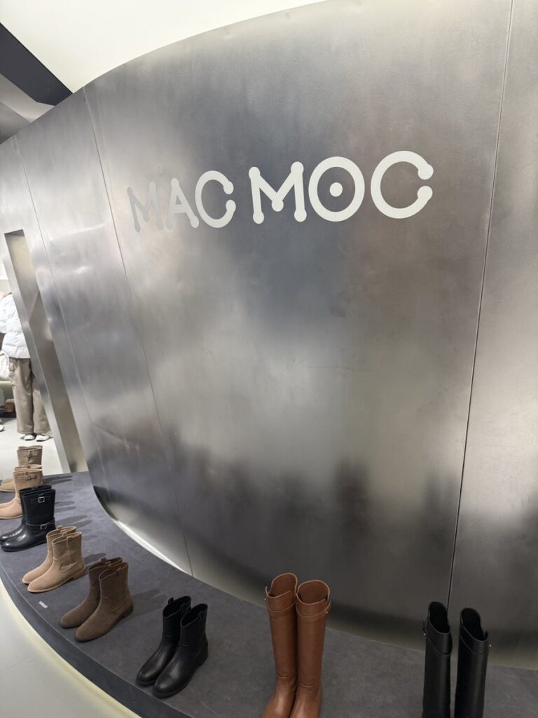 Brushed-steel wall with the MAC MOC logo and boots on display
