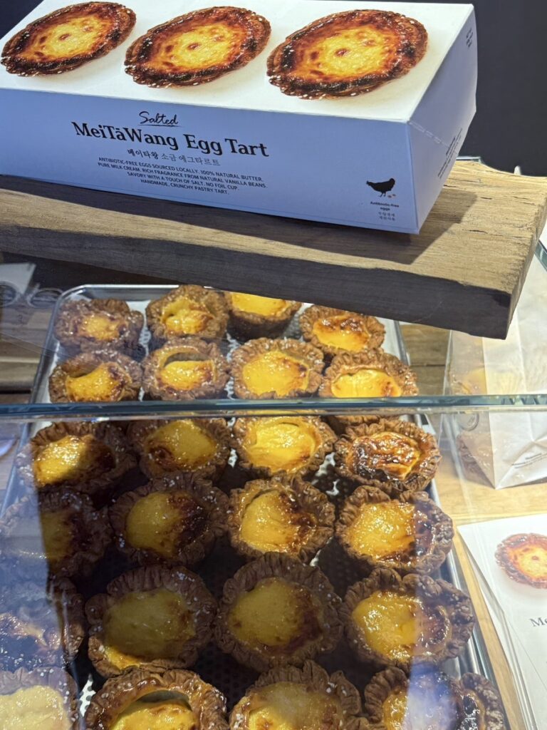 White MeiTaWang gift box above trays of egg tarts