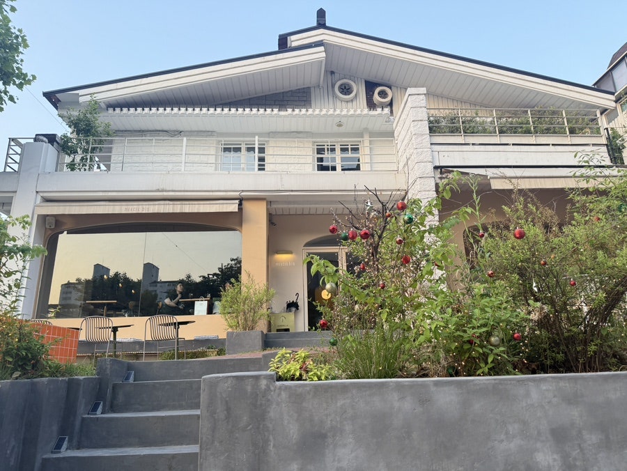 White house-style building of Mercer bis Café behind a green garden