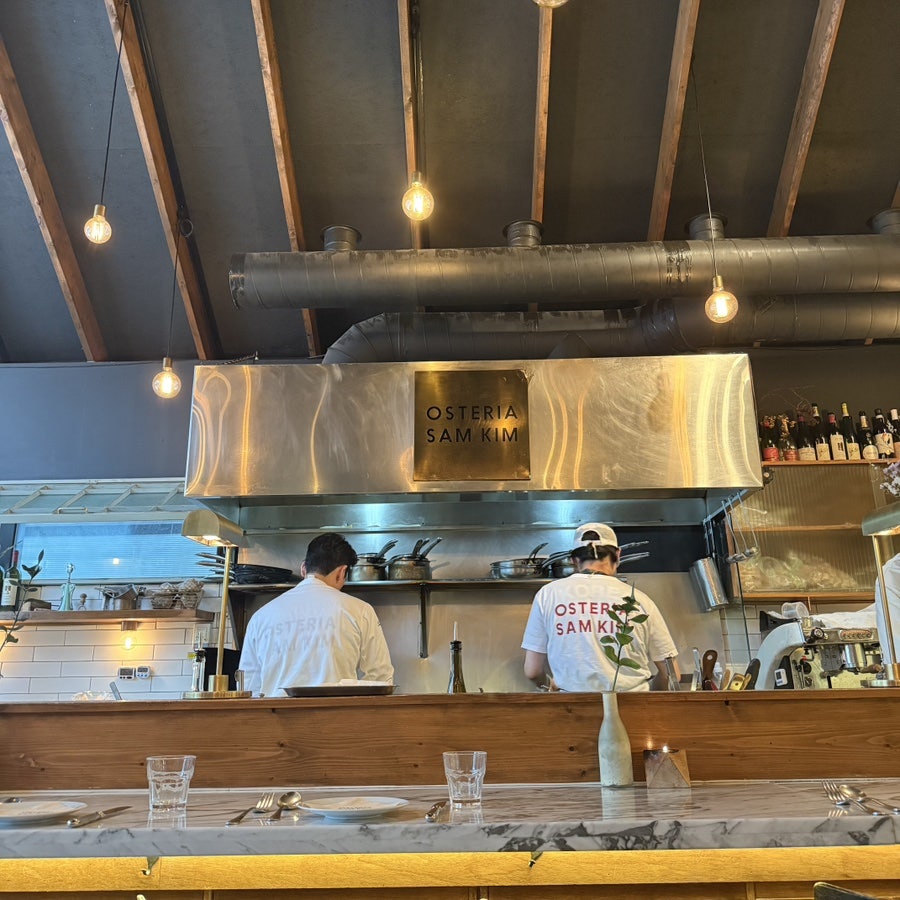 Open kitchen with stainless hood and the Osteria Sam Kim sign