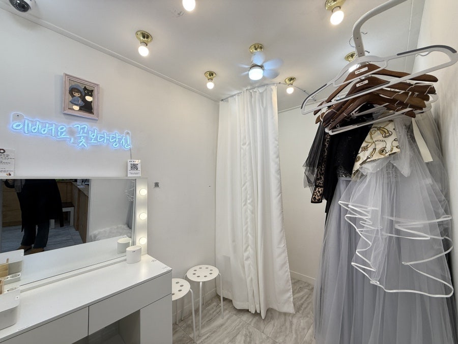 Makeup room with a lit vanity mirror next to a rack of dresses