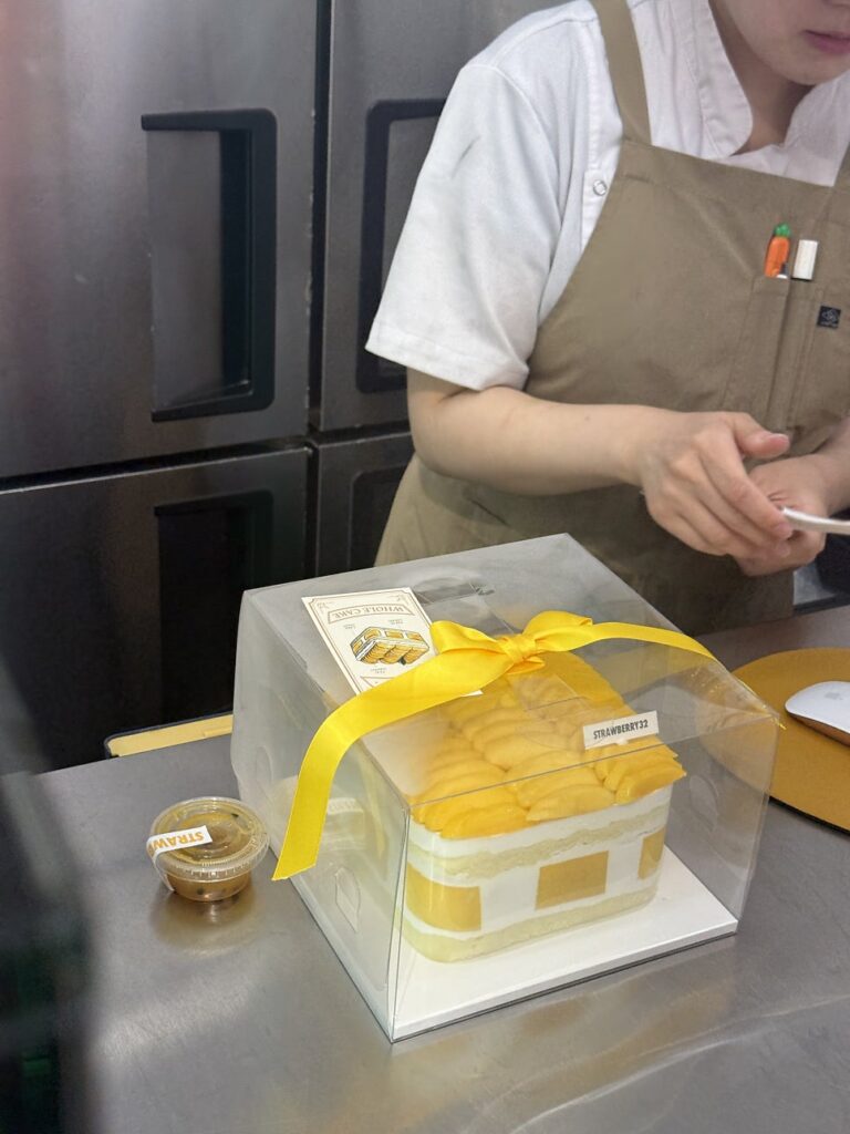 Staff packing the mango cake with a yellow ribbon and sauce cup