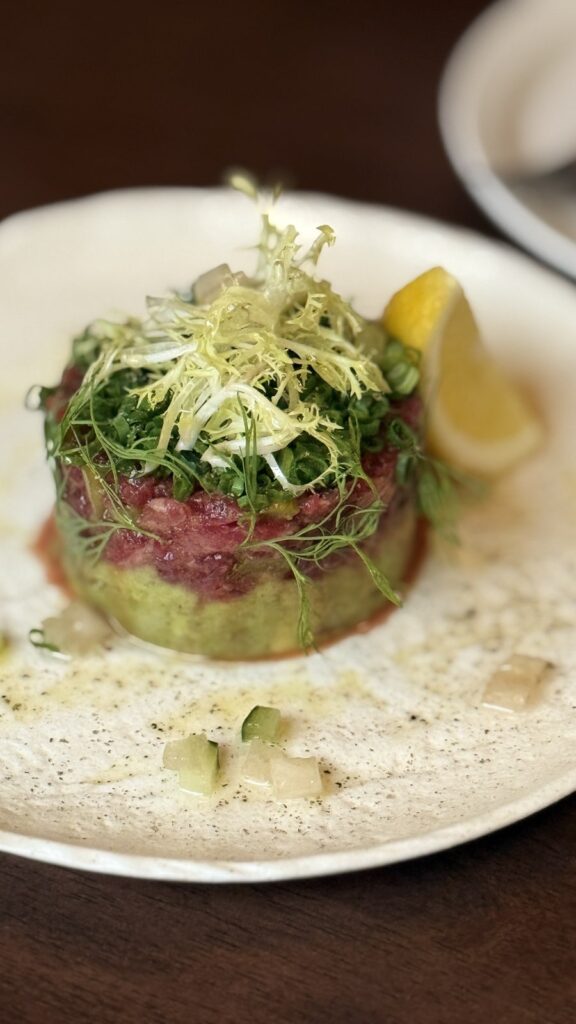 Avocado beef tartare topped with greens and a lemon wedge